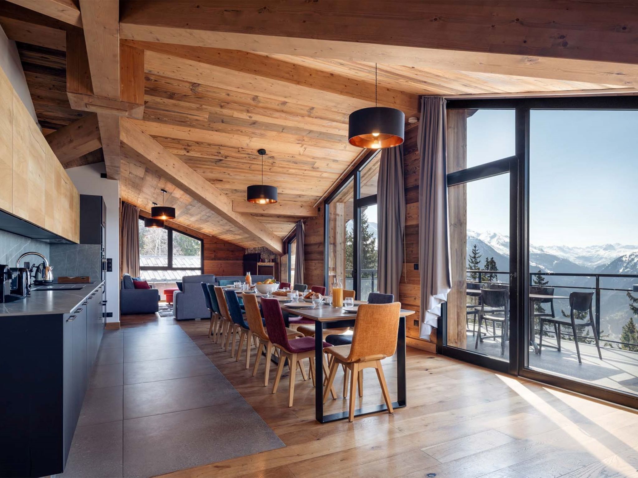 A modern kitchen with a long counter, wooden cabinets, and a large window overlooking a mountainous landscape.