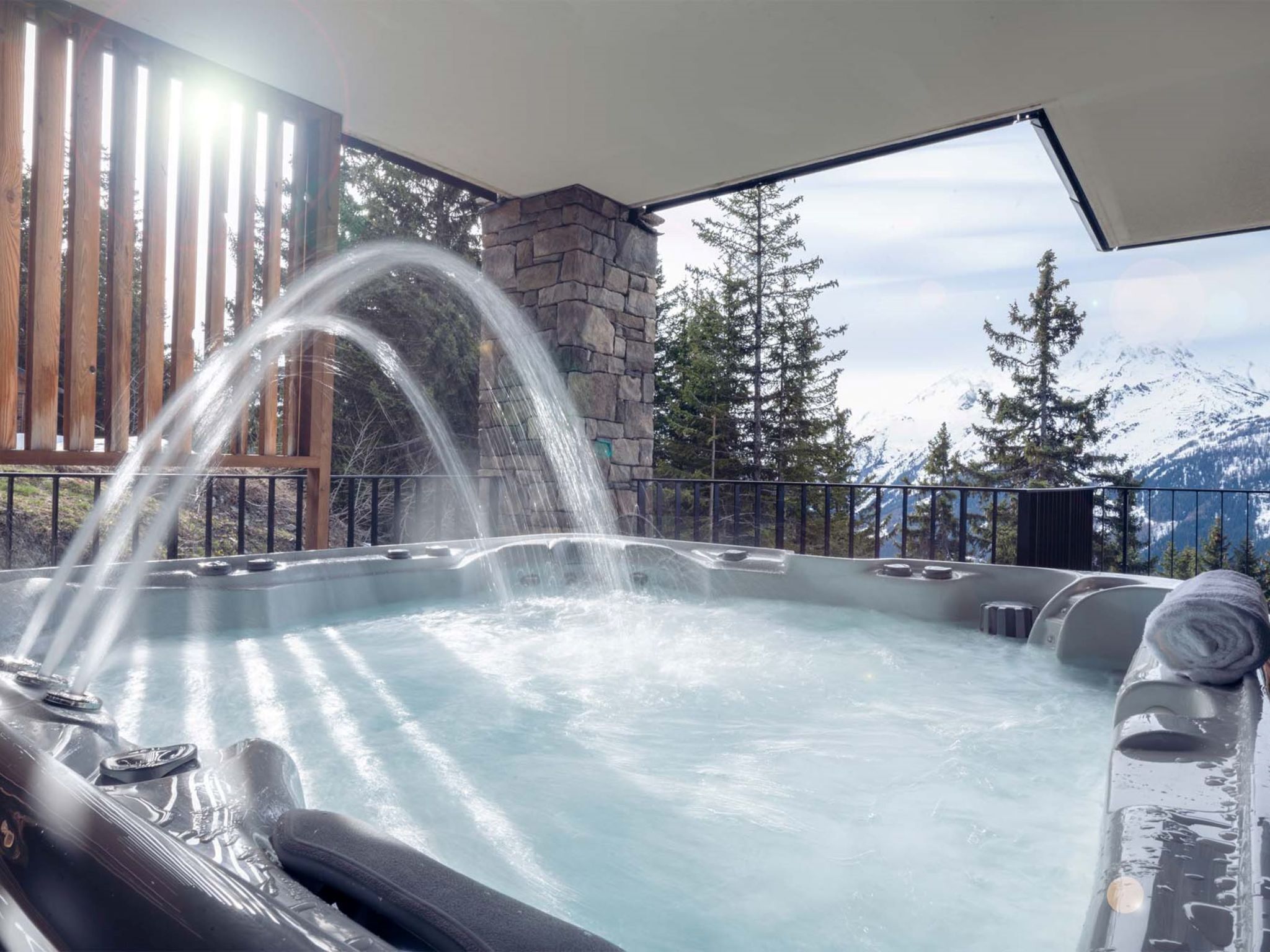 Un jacuzzi con chorros de agua, rodeado por un muro de piedra y una terraza de madera, con vistas a la montaña de fondo.