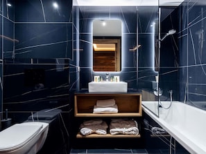 Une salle de bain moderne avec un sol en marbre, un meuble-lavabo en bois, un lavabo blanc, un miroir, une douche et des toilettes.