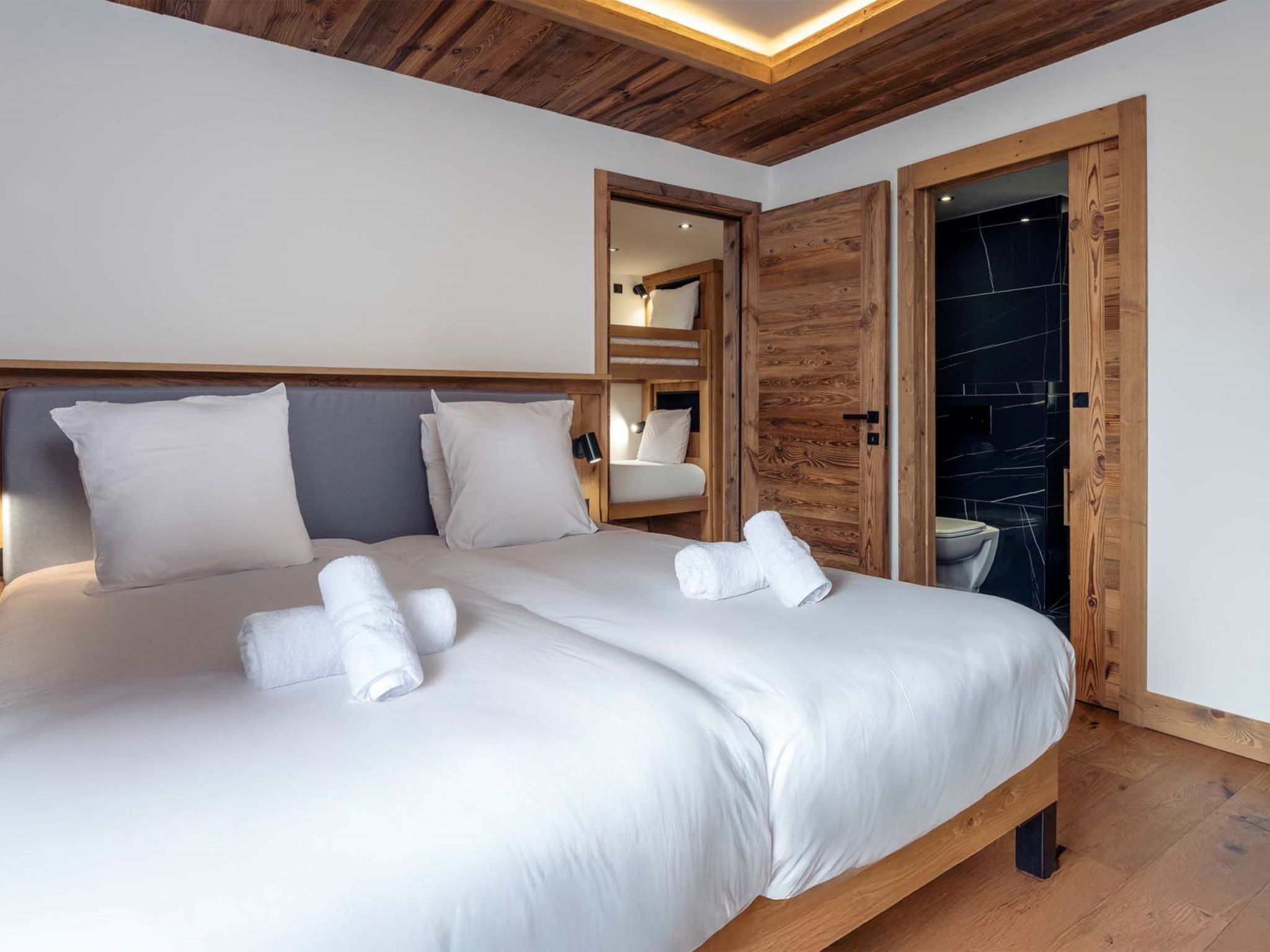 Een moderne slaapkamer met een houten plafond, een groot bed met witte lakens en een houten deur naar een badkamer.