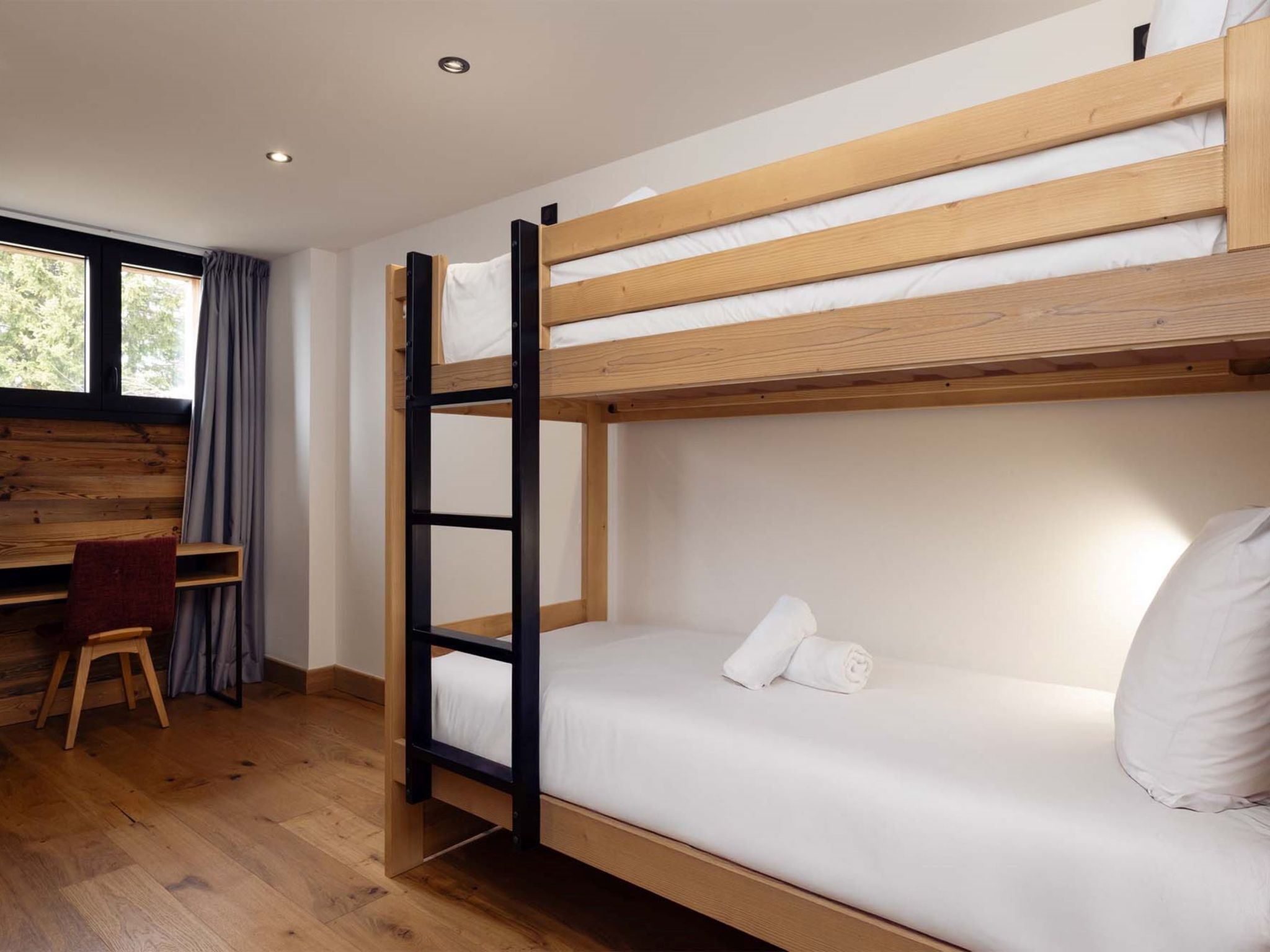 Un lit superposé avec un bureau et une chaise, un plancher en bois et une fenêtre avec des rideaux.