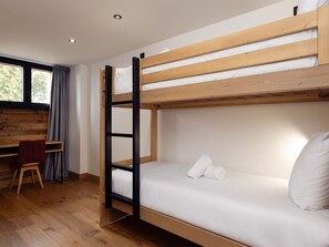 Un lit superposé avec un bureau et une chaise, un plancher en bois et une fenêtre avec des rideaux.