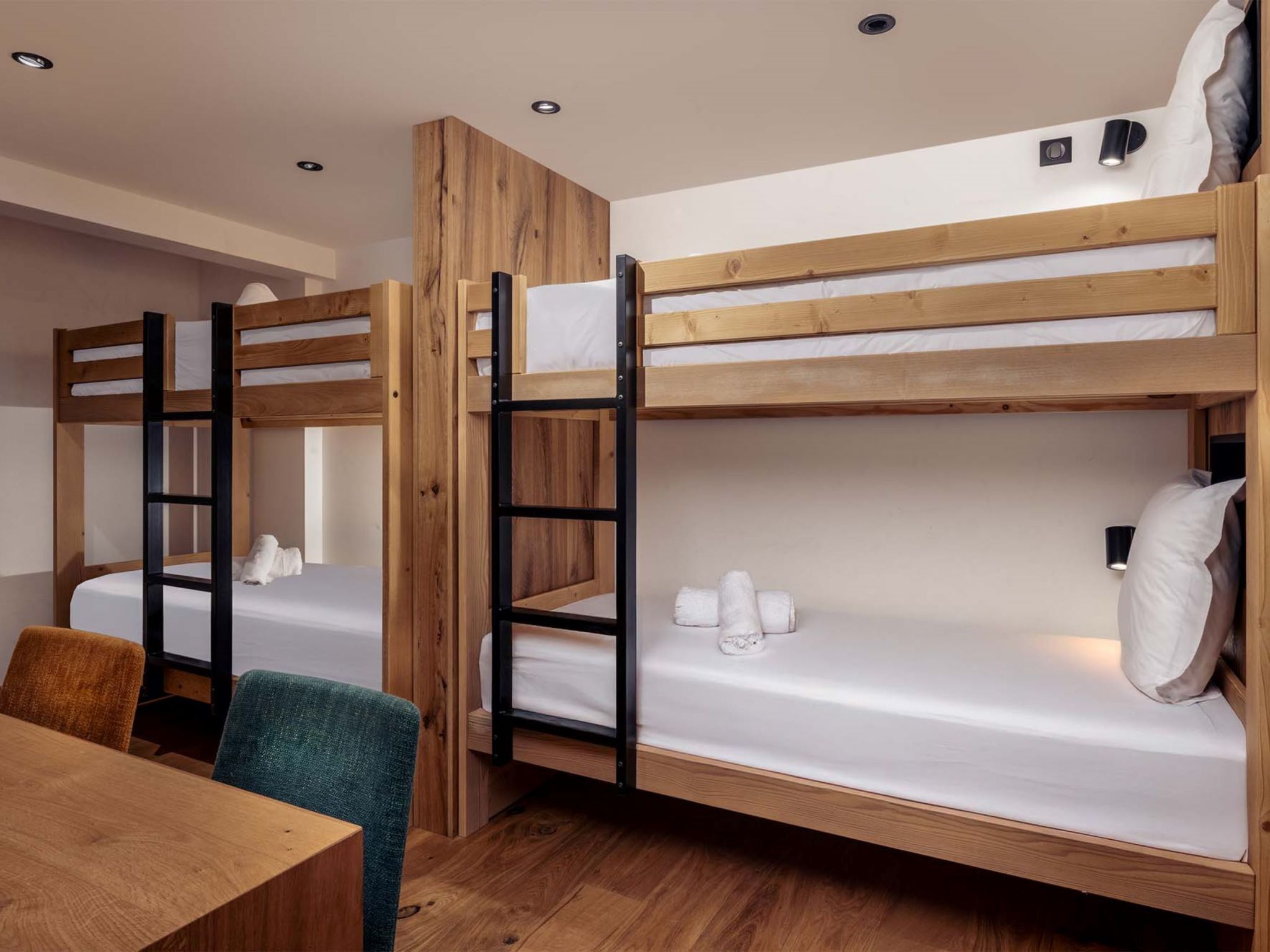Une chambre avec un lit superposé, une table et des chaises en bois, un petit bureau et un luminaire fixé au mur.