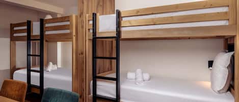 Une chambre avec un lit superposé, une table et des chaises en bois, un petit bureau et un luminaire fixé au mur.