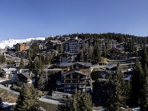 Une station de montagne composée de plusieurs bâtiments en bois, dont certains sont dotés de balcons, et entourée d’arbres et de montagnes aux sommets enneigés.