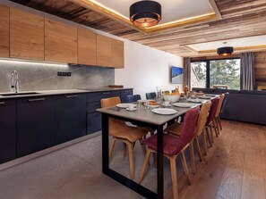 A modern kitchen with dark cabinets, a stainless steel sink, and a dining area with a wooden table and chairs. - Résidence l'Orée du Bois by Interhome (La Rosière)