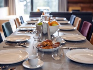 Una mesa de comedor dispuesta con platos, cubiertos, vasos y un bol de fruta.