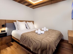 Habitación de hotel con techo de madera, cama con ropa blanca, mesita de noche con lámpara y suelo de madera.