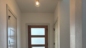 A hallway with a wooden door, white walls, and a hanging light fixture. - Newly Built Home 7 Min Drive River Walk & Downtown - 1222 (San Antonio)