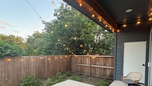 A covered patio with a concrete floor, two wicker chairs, and a wooden fence. - Newly Built Home 7 Min Drive River Walk & Downtown - 1222 (San Antonio)