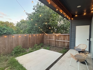 Eine überdachte Terrasse mit Betonboden, zwei Korbstühlen und einem Holzzaun.