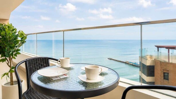 Un balcone con un tavolino in vetro, due tazze bianche e un vaso con pianta.