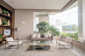 A modern living room with a sofa, two armchairs, a glass coffee table, and a large window with a view of the city. - Ocean View Luxury Apt | King Bed |Walk to Larcomar (Miraflores)