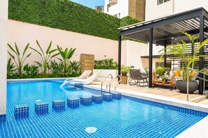 A swimming pool with steps, lounge chairs, and a covered seating area with plants. - Ocean View Luxury Apt | King Bed |Walk to Larcomar (Miraflores)