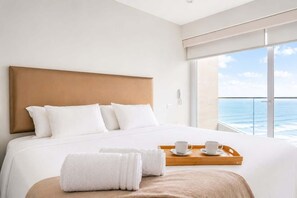 A hotel room with a large bed, white bedding, a wooden headboard, a wooden tray with a cup and saucer, and a view of the ocean. - Ocean View Luxury Apt | King Bed |Walk to Larcomar (Miraflores)