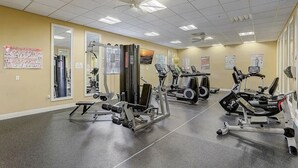 Un gimnasio con diversos equipos de ejercicio, espejos y carteles informativos en las paredes.