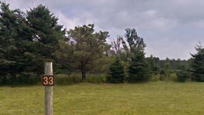 Un poteau en bois portant le numéro 33, situé dans un champ herbeux avec des arbres en arrière-plan.
