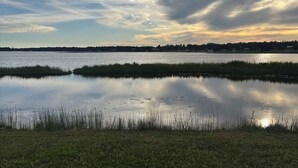 Un lac paisible, bordé de rives verdoyantes, avec une ligne d’arbres qui se dessine à l’horizon sous un ciel nuageux.