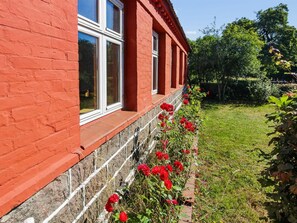Ein Gebäude aus roten Ziegeln mit weiß gefassten Fenstern und einem Garten mit roten Blumen.