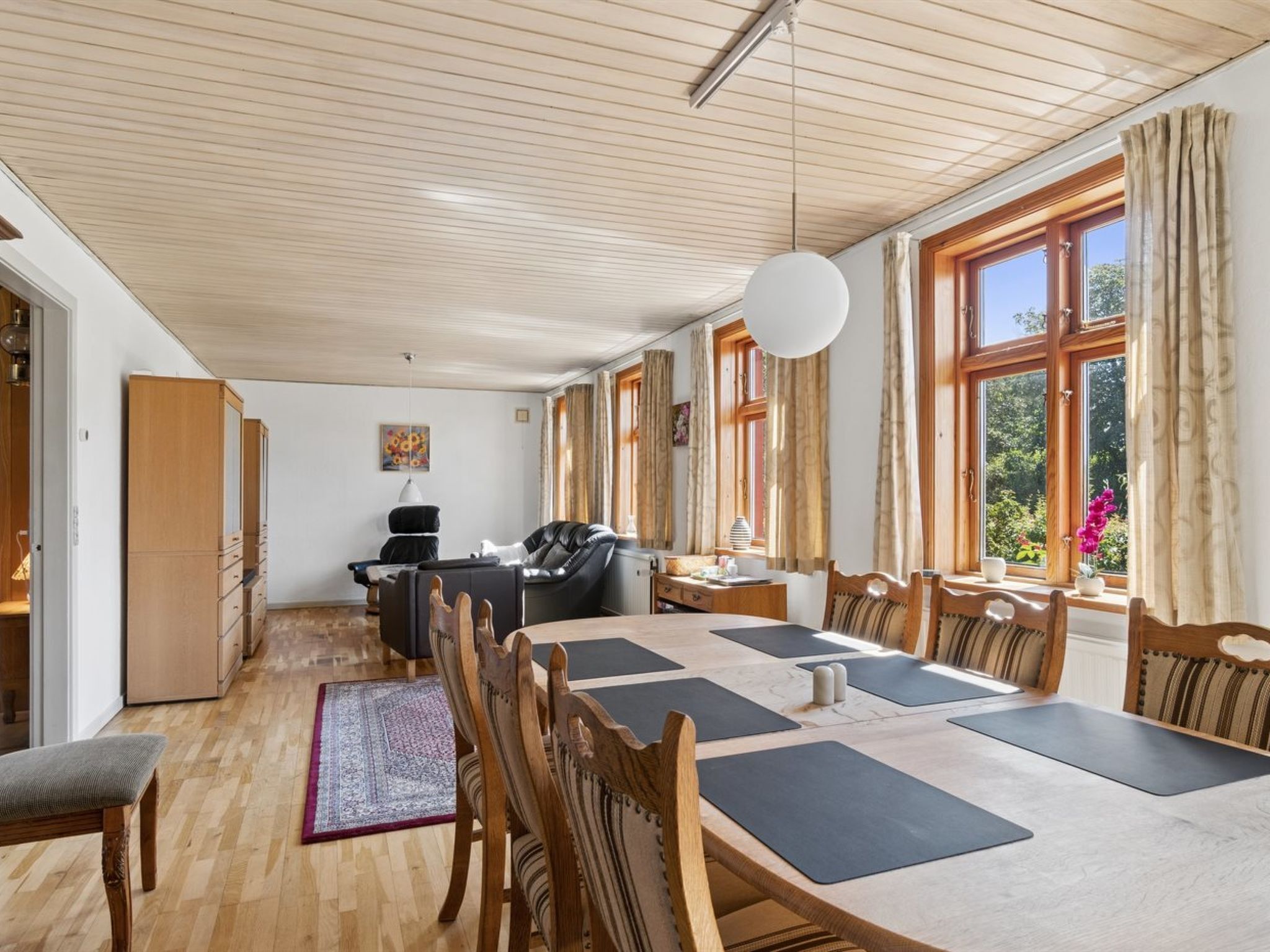 A spacious room with a large table, chairs, a sofa, and a wardrobe.