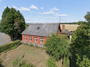 Ein rotes Backsteinhaus mit einem Ziegeldach, umgeben von viel Grün und einem Feld.