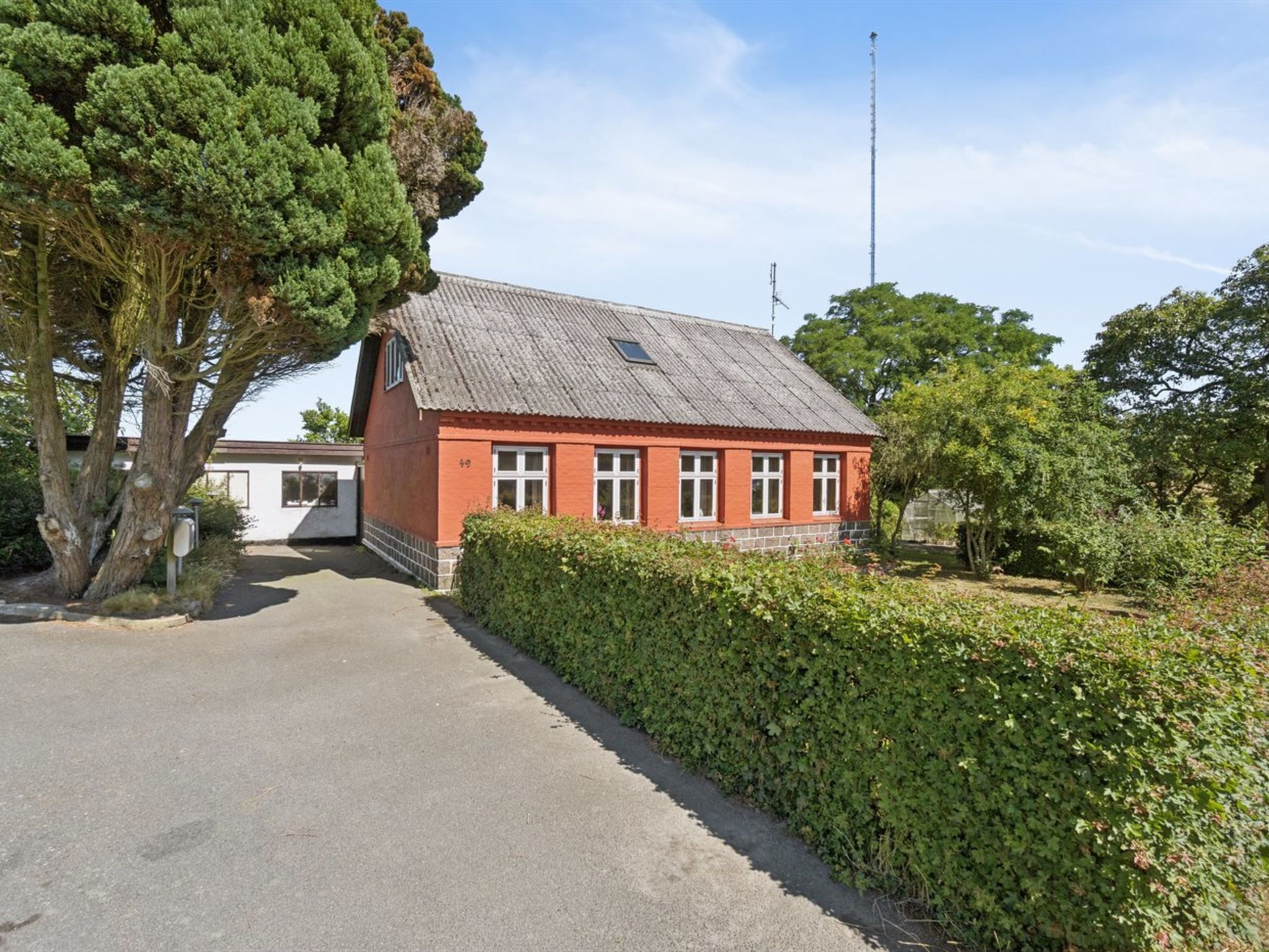 En byggnad med röda tegelväggar och ett sluttande tak, en asfalterad uppfart och en häck framför.