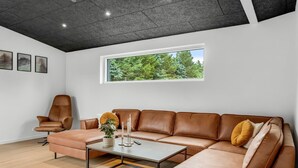 Ein modernes Wohnzimmer mit einer Ledersofa, einem Couchtisch und einem großen Fenster mit Blick auf Bäume.
