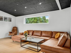 A modern living room with a leather sofa, a coffee table, and a large window with a view of trees. - "Lillesol" - 1.3km from the sea by Interhome (Hjørring)