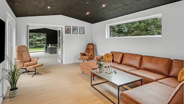 Ein modernes Wohnzimmer mit einer Ledersofa, einem Couchtisch und Blick auf einen Wald durch ein großes Fenster.