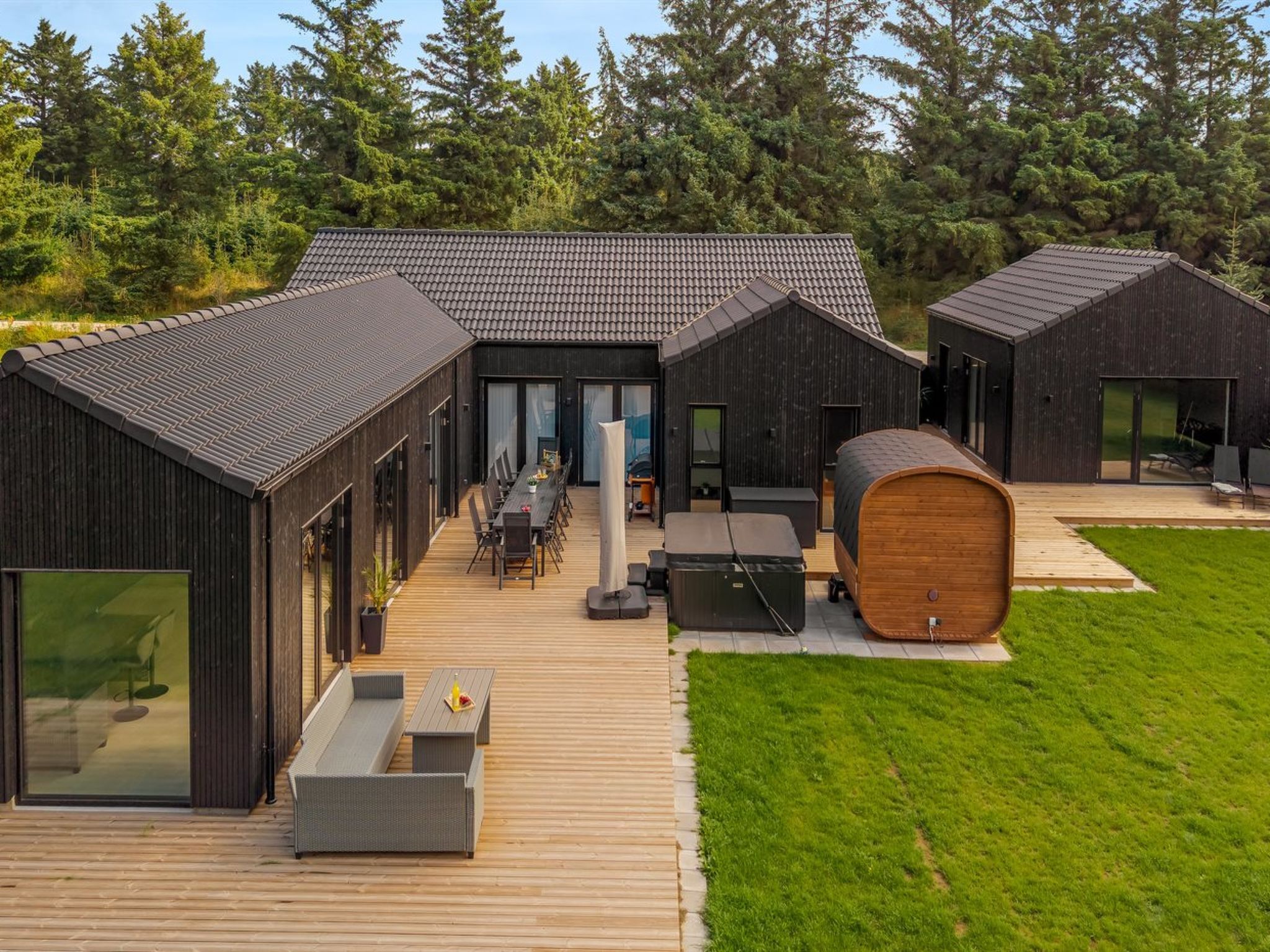 Een modern huis met een houten terras, zitplaatsen buiten en een grote ton.