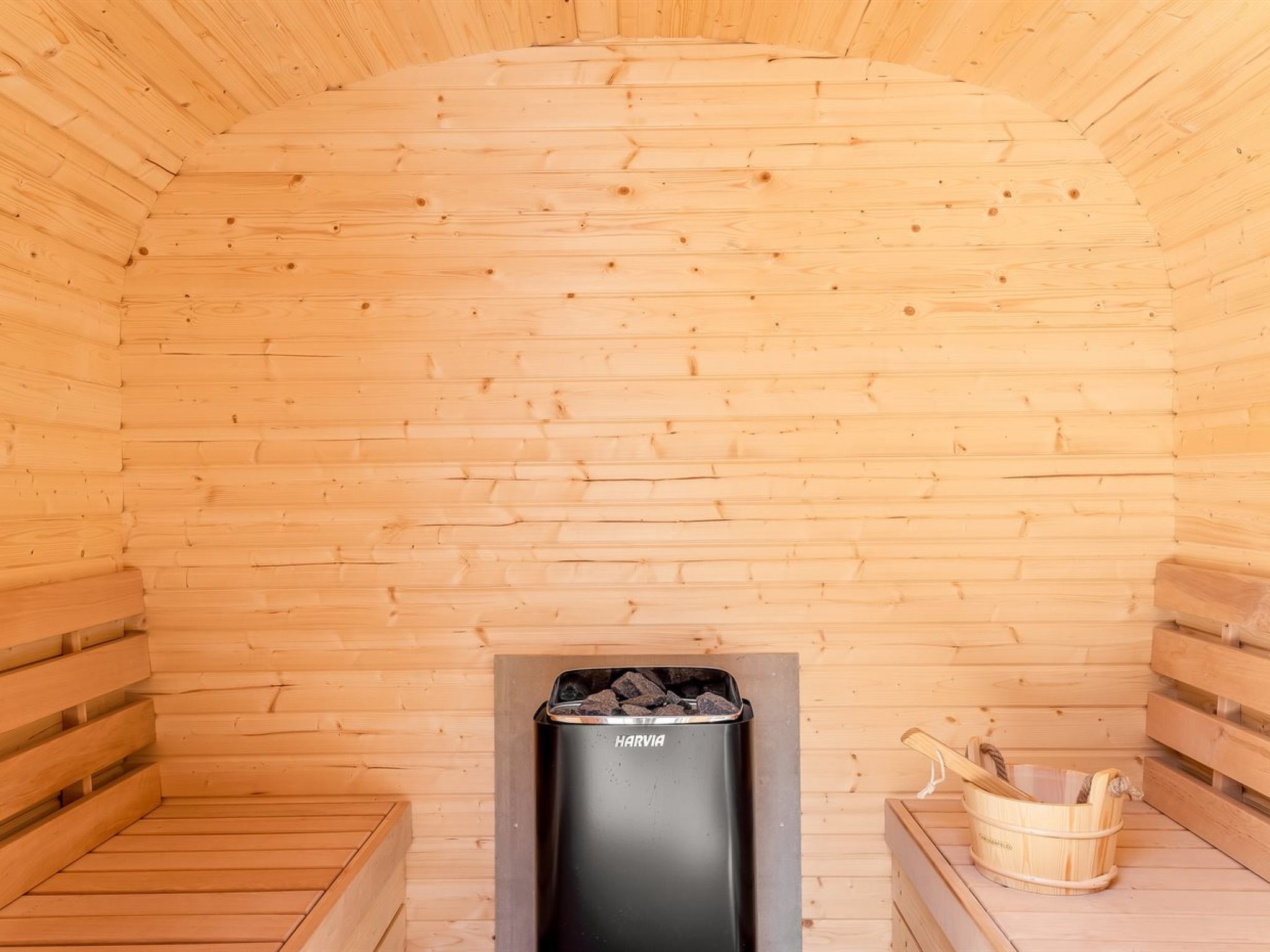 Ein Saunaraum mit Holzwänden und -bänken, einer Harvia Saunaanlage und einem Holz-Eimer.