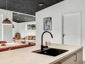 Une cuisine moderne avec un évier noir, des luminaires suspendus et un coin repas agrémenté d’un canapé en cuir marron.