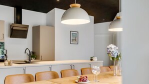 Ein zeitgemäßer Essbereich mit einem Holztisch, sechs Stühlen, zwei Pendelleuchten, einer Blumenvase und einer Schale mit Trauben.