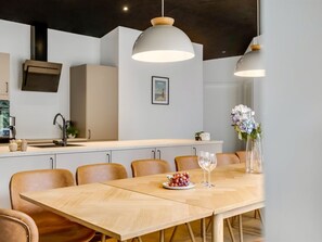 A modern dining area with a wooden table, six chairs, two pendant lights, a vase with flowers, and a plate of grapes. - "Lillesol" - 1.3km from the sea by Interhome (Hjørring)