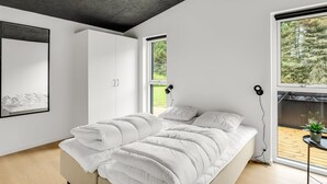 Ein modernes Schlafzimmer mit einem großen Bett, einem Kleiderschrank und einem Fenster mit Blick auf Bäume.