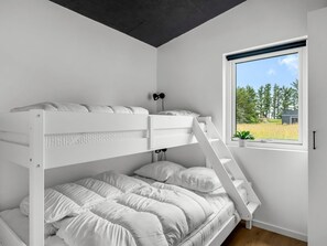 Une chambre avec un lit superposé, dont la fenêtre donne sur un champ verdoyant et des arbres.