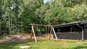 Puinen keinuteline ruohikkoisella alueella, taustalla näkyy puinen mökki.