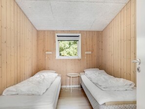 Een eenvoudige, kleine kamer met twee bedden, een raam en een klein tafeltje.