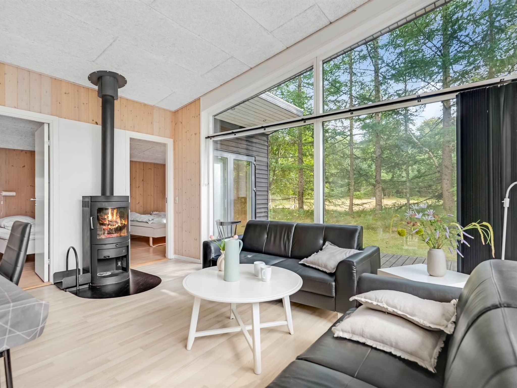 A modern living room with a wood-burning stove, a sofa, a coffee table, and large windows offering a view of the outdoors.