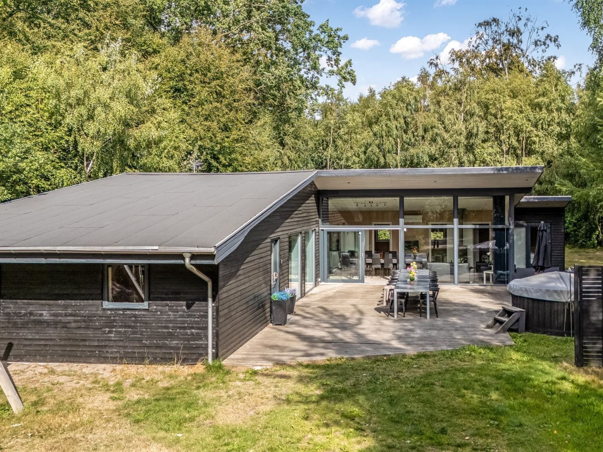 A modern house with a flat roof, large windows, and a patio with outdoor furniture.