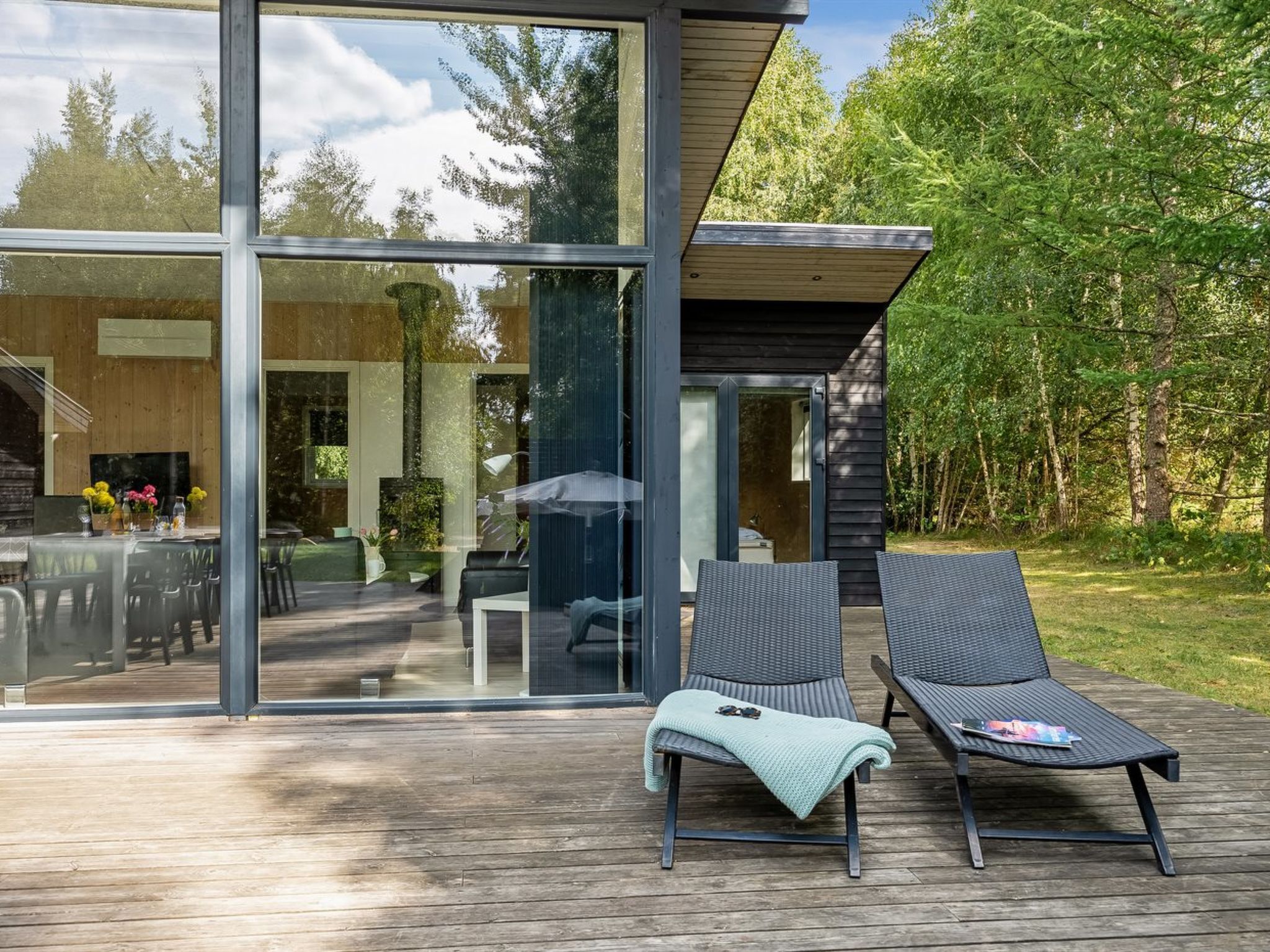 A modern outdoor deck with two lounge chairs and a dining area visible through large glass doors.