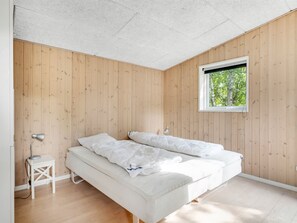 A bedroom with a wooden wall, a single bed, a bedside table, and a window with a view of trees. - "Nakke" - 900m from the sea by Interhome (Hadsund)