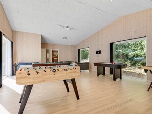 Een moderne woonkamer met een tafelvoetbaltafel, een poolbiljart en een biljarttafel. Een groot raam biedt uitzicht op het omliggende landschap.