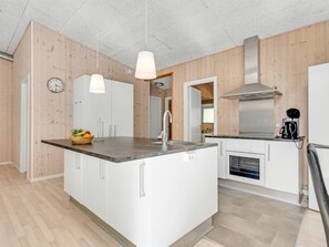Een moderne keuken met een centraal eiland, witte kasten, een roestvrijstalen afzuigkap en een klok aan de muur.