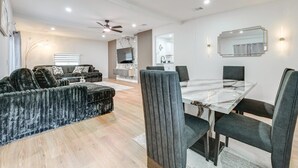 A modern living room with a sofa, a dining table with chairs, a TV, and a kitchen area in the background.