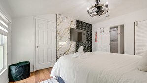 A modern bedroom with a large bed, a flat-screen TV, a ceiling light fixture, and a door with a geometric-patterned wall.