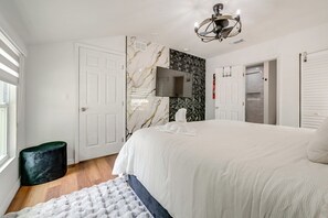 A modern bedroom with a large bed, a flat-screen TV, a ceiling light fixture, and a door with a geometric-patterned wall.