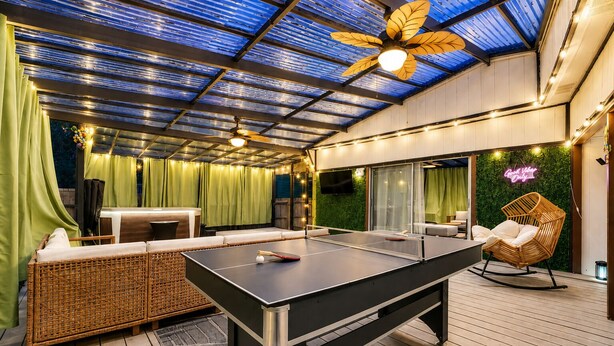 An outdoor area with a ping pong table, wicker furniture, and a ceiling fan.