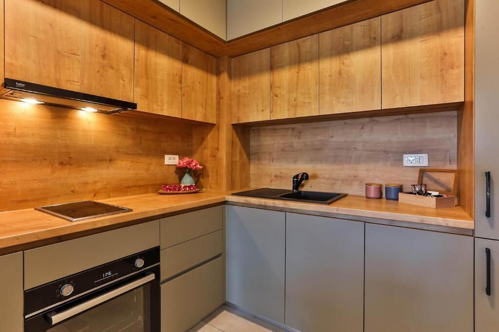 Cocina moderna con armarios de madera, horno empotrado, un lavamanos y una encimera con un florero y utensilios.