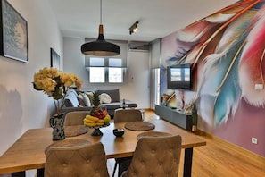 A dining area with a wooden table, cushioned chairs, a vase with flowers, and a fruit bowl.